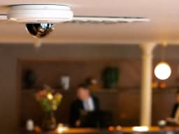 M5075 camera witch is white and black with the AXIS LOGO is handing from the celing in of a hotel lobby from AXIS COMMUNICATIONS